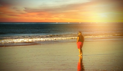 Ältere Dame geht einsam am Strand bei Sonnenuntergang