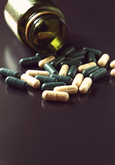 Angle view of pill bottle with green and white prescription medicine spilling across a black background a lot of space for text