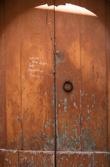 Old abandoned door scratched, rusty knocker . With graffiti, dedications and memories. Arch and light beam.
