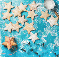 Christmas or New Year holiday food background. Sweet gingerbread cookies in shape of star with sugar powder and metal shapes on blue painted plywood background, top view