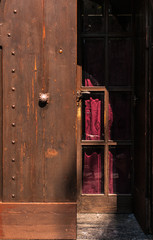 Old wooden studded door, opened a half. Inner door closed with red curtain purple. Attention Do not open.