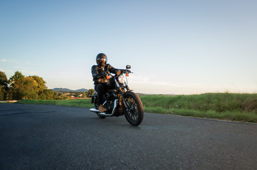 Fototapeta na wymiar Man sat on motorcycle on the road during sunset. Chopper high power motorcycle goes over landscape.
