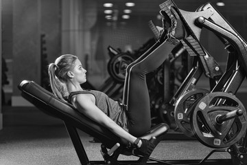 Sportive woman using weights press machine for legs at the gym. Pretty brunette exercising in a...