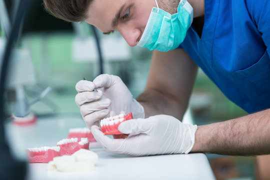 Dental prosthesis, dentures, prosthetics work. Prosthetics hands while working on the denture, false teeth, a study and a table with dental tools.