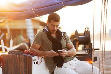 Handsome man using cellphone on sailing boat in sunset