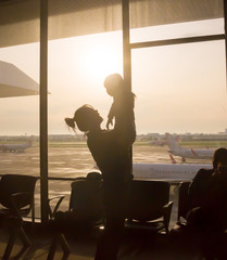 Silhouette of  Mother raising her little daughter up high at airport with airplane is background 