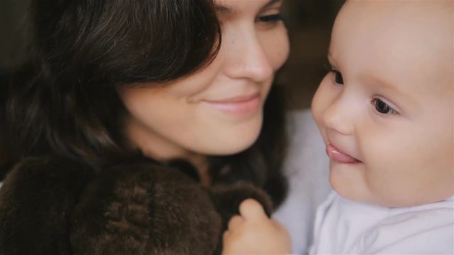 Young Happy Mother Holding her Newborn Child and kissing. Family at home. Beautiful smiling Mom and Happy Baby Together. Tenderness concept.