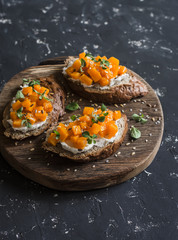 Pumpkin and goat's cheese bruschetta on a wooden cutting board on dark background. Healthy vegetarian snack