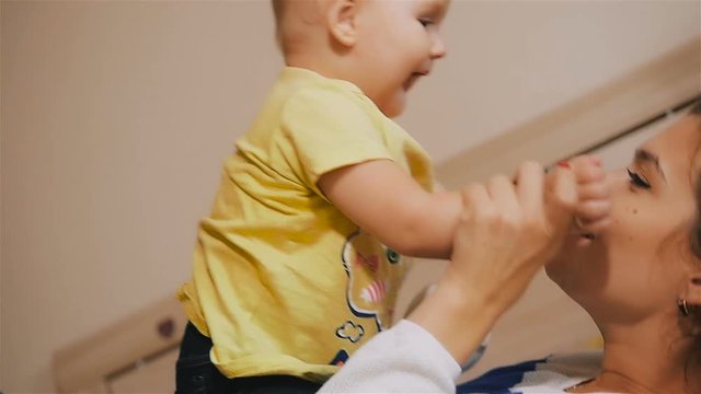 Young Happy Mother Holding her Newborn Child and throws up. Family at home. Beautiful smiling Mom and Happy Baby Together in bed.