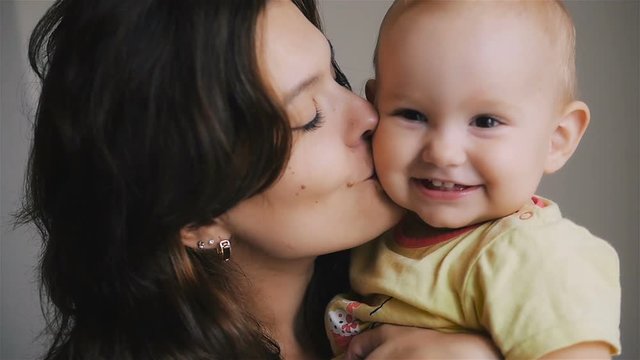 Young Happy Mother Holding her Newborn Child. Family at home. Beautiful smiling Mom and Happy Baby Together.