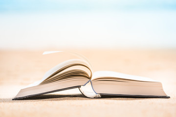opened pages of book on sand at beach, selective focus