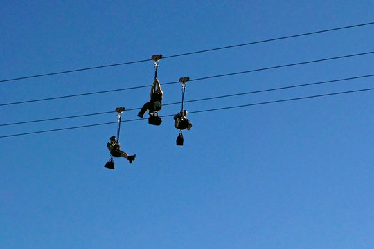 Silhouette von drei Personen an einer Zipline gegen blauen Himmel