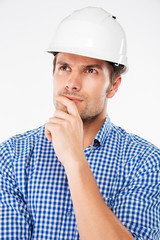 Pensive young man building engineer in helmet standing and thinking