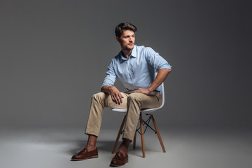 Pensive brunette man in blue shirt sitting on the chair