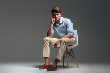 Pensive brunette man in blue shirt sitting on the chair