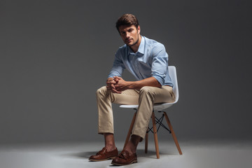 Pensive brunette man in blue shirt sitting on the chair