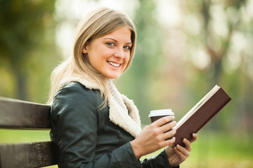 Fototapeta premium Young woman is reading book and drinking coffee to go.