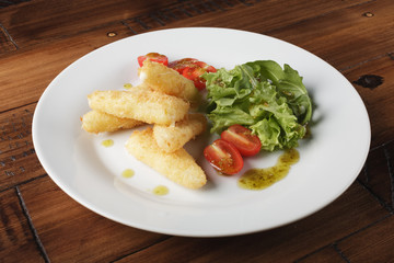 Breaded cheese (deep-fry) with tomatoes and greens in a white plate. Wooden background