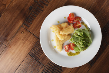 Breaded cheese (deep-fry) with tomatoes and greens in a white plate. Wooden background