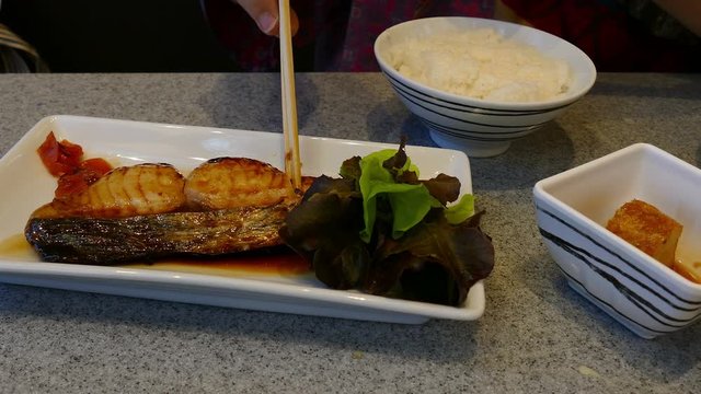 woman's hand using chopstick to eat grilled mackerels fish - japanese food