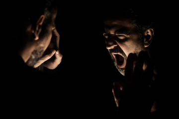 Angry man shouting in front of mirror at his reflection in a dark room
