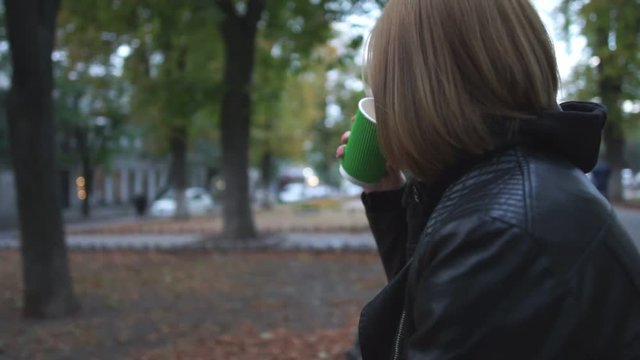 Young woman drinks coffee in the street at the evening