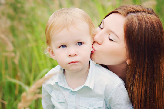 Mom tenderly kissing baby son in the ear, nature, close-up.