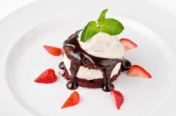 Dessert with chocolate sponge cake, vanilla cream, cherry, ice cream and strawberries on a plate on a white background, close up