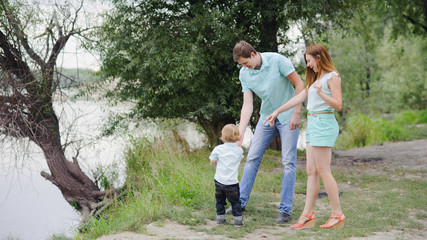 Mom, dad and son walk in nature on a river, turquoise dresses, full length view.