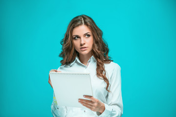 Fototapeta premium The thoughtful young business woman with pen and tablet for notes on blue background