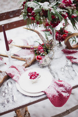 Obraz na płótnie Canvas Wedding table setting in marsala colors with plates, cutlery, red floral compositions, candles, velvet napkins, deer horns on table covered with snow