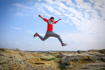 Sportsman running, jumping over rocks in mountain area.