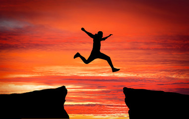 Fototapeta premium Man jumping across the gap from one rock to cling to the other.
