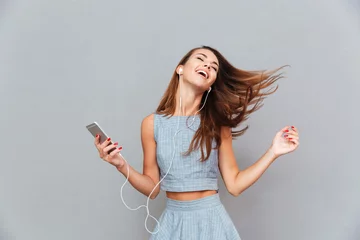 Fotobehang Happy carefree woman dancing and listening to music from smartphone © Drobot Dean