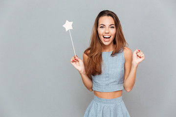 Happy amazed young woman holding magic wand - obrazy, fototapety, plakaty