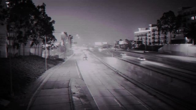 A monochromatic "security cam" video of a freeway at night.