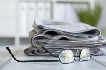 Stack of newspapers and eyeglasses