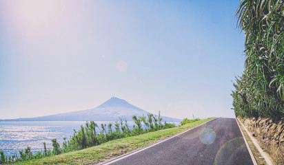 asphalted road in Azores runs along the grassy shores of the Atlantic Ocean, on a background of of an extinct volcano and the blue sky