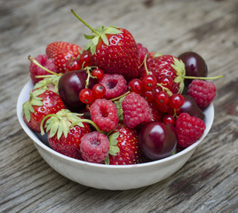 Ripe fruit and berries in a white cup on a wooden table