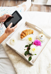 Beautiful woman using a tablet with breakfast in bed, detail