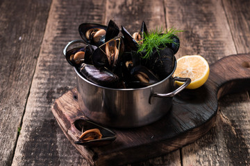 Mussels in copper cooking dish and lemon on dark wooden background