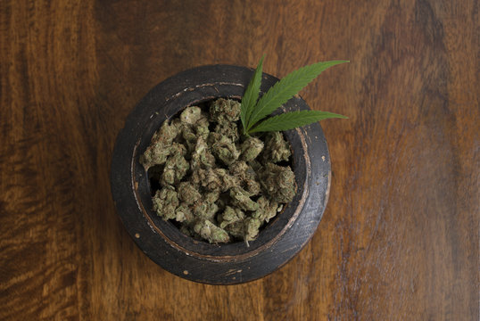 Cannabis sativa flower buds and leaf in wooden pot, on wooden background