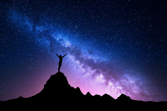 Landscape with Milky Way. Colorful night sky with stars and silhouette of a standing happy woman with raised-up arms on the mountain peak on the background of beautiful galaxy. Blue milky way rocks