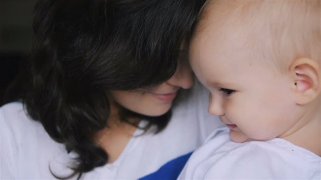 Young Happy Mother Holding her Newborn Child and kissing. Family at home. Beautiful smiling Mom and Happy Baby Together. Tenderness concept.