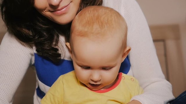 Young Happy Mother Holding her Newborn Child and throws up. Family at home. Beautiful smiling Mom and Happy Baby Together in bed.
