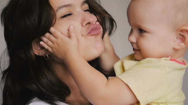 Young Happy Mother Holding her Newborn Child. Family at home. Beautiful smiling Mom and Happy Baby Together.