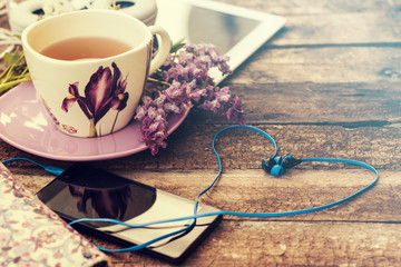 still life with tea cup and the contents of a work space composed. Different objects on wooden table. tablet,phone with headphones and spring flowers