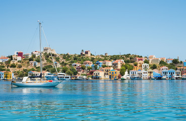 Fototapeta na wymiar View over bay of Kastelorizo on sunny summer day. Island coast with typical colorful Greek houses, clear turquoise sea water and yacht. Dodecanese, Greece
