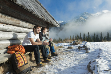 Two friends relaxing on wooden bench in winter mountains outdoors