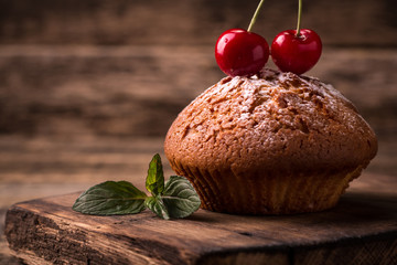 Tasty muffin with cherry and mint on vintage wooden background